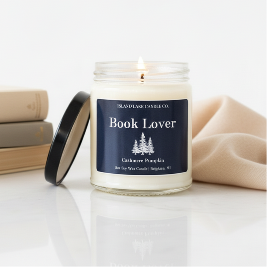 Book Lover candle by Island Lake Candle Co. on white background with stacked neutral books and soft cashmere fabric